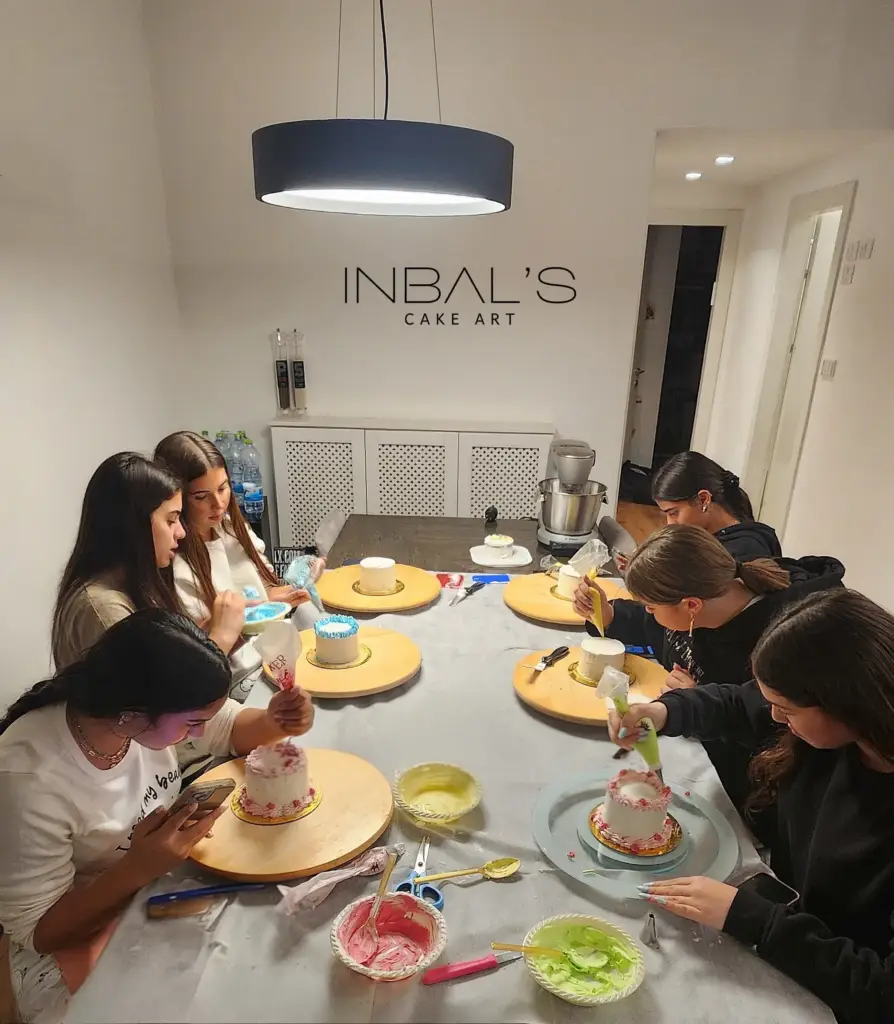 ילדות יושבות מסביב לשולחן גדול ומכינות עוגות בנטו בסדנה של ענבל שלו