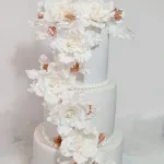 עוגת חתונה מעוצבת בשלוש שכבות עם פרחים לבנים וזוהרים, מתאימה לאירועים מיוחדים.